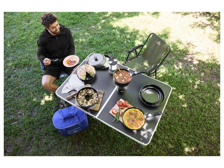 Homme en camping avec table portable remplie de nourriture et d'ustensiles, dont des poêles et un sac isotherme.