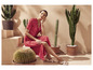 Une femme en robe rouge à fleurs et sandales blanches pose à côté de cactus.