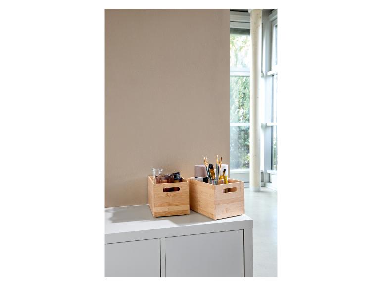 Boîtes en bambou avec fournitures d'art et petits objets sur un meuble blanc.