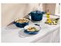 Casseroles en fonte bleues avec repas et planche à découper sur un comptoir blanc.