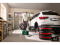 Homme changeant les pneus de voiture dans un garage avec un compresseur d'air portable et des housses de pneus.