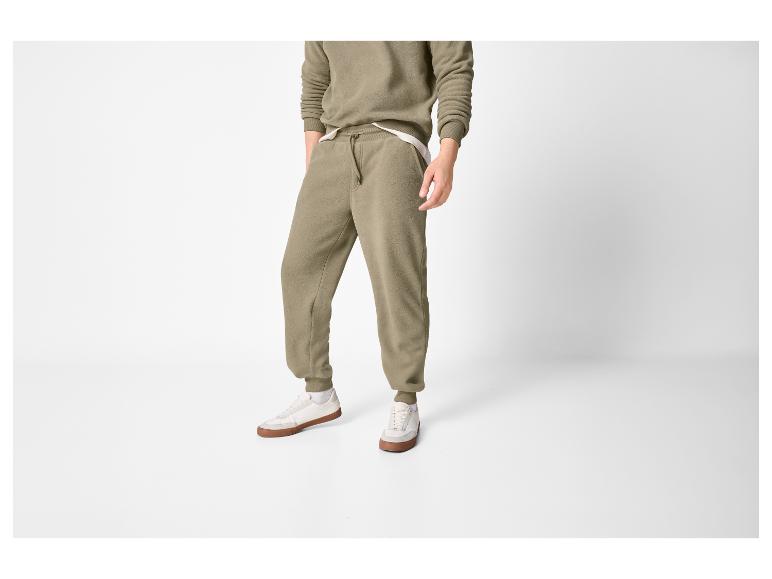 Homme en survêtement kaki, avec pantalon de survêtement et sweat-shirt, portant des baskets blanches.