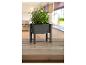Un pot de fleurs en bois noir avec des herbes sur une table en bois.