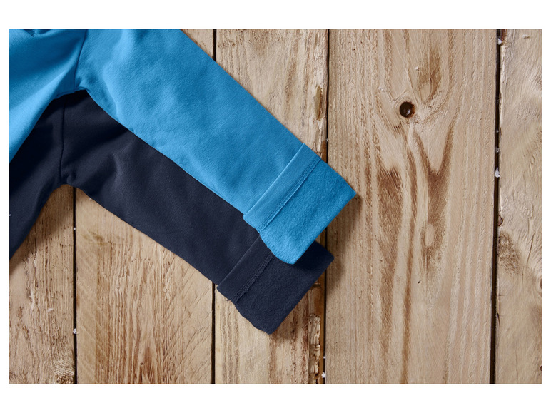 Manches bleues et bleu foncé d'un pull sur un fond en bois.