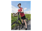 Une femme avec un casque de vélo se tient à côté de son vélo électrique noir sur une route de campagne.
