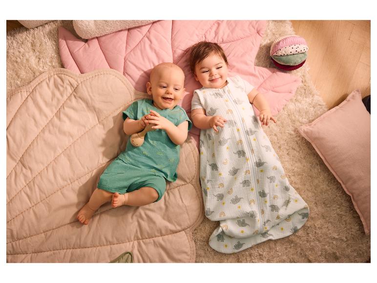 Deux bébés souriants allongés sur des tapis de jeu roses, l'un dans une gigoteuse, l'autre dans une tenue verte.
