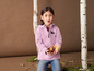 Une jeune fille portant une veste rose tient des feuilles d'automne.