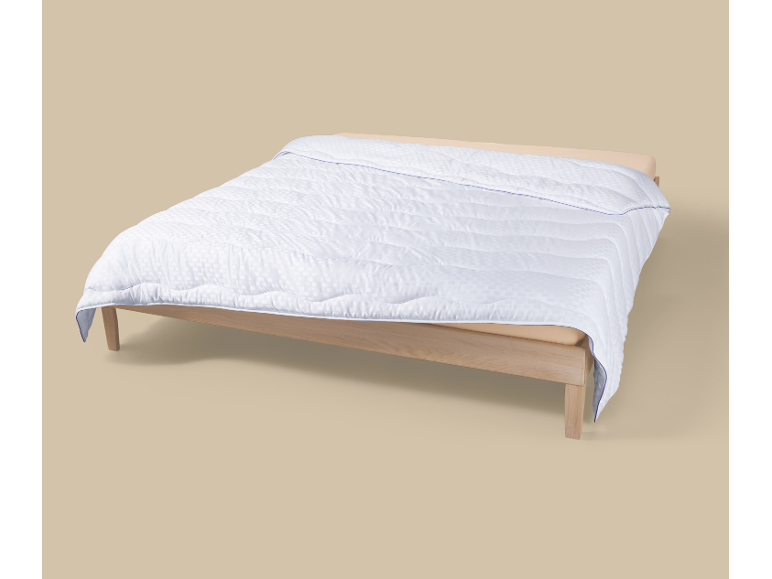 Couette blanche matelassée avec motif sur un lit en bois.