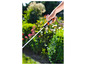 Une main tient un tuyau d'arrosage Gardena et arrose un jardin vert.