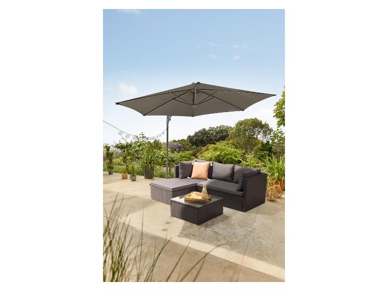 Salon de jardin d'angle en rotin avec coussins, table basse en verre et grand parasol gris.