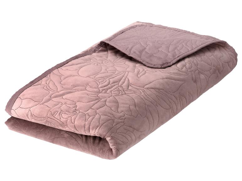 Une couverture matelassée pliée de couleur rose poudré avec un motif floral en relief.