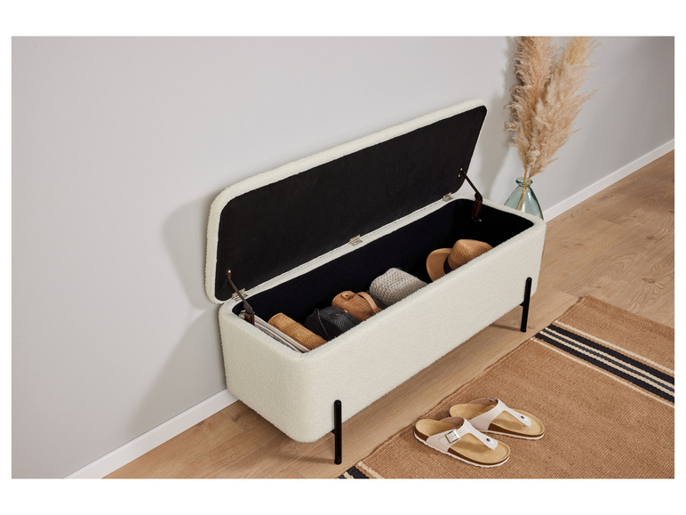 Un banc de rangement blanc avec le couvercle ouvert, rempli d'accessoires comme des sacs et un chapeau.