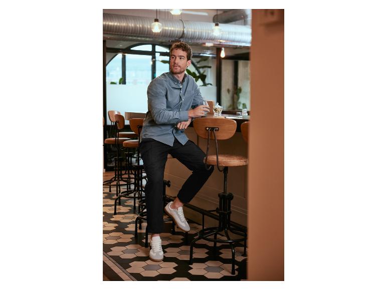 Homme en chemise bleu clair et baskets blanches assis sur un tabouret de bar dans un café.
