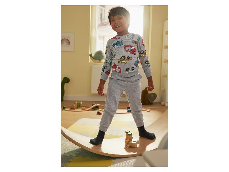Un garçon portant un sweat-shirt gris à motifs de voitures joue sur une planche d'équilibre en bois.