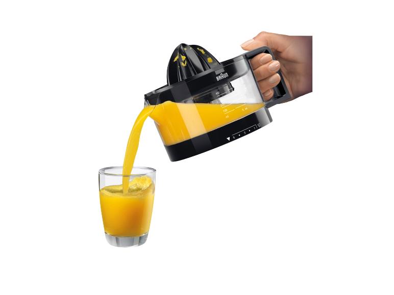 Main versant du jus d'orange fraîchement pressé d'un presse-agrumes dans un verre.