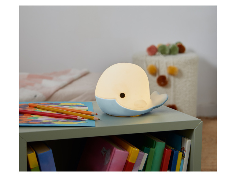 Une lampe de chevet bleue en forme de baleine sur une table de chevet verte.