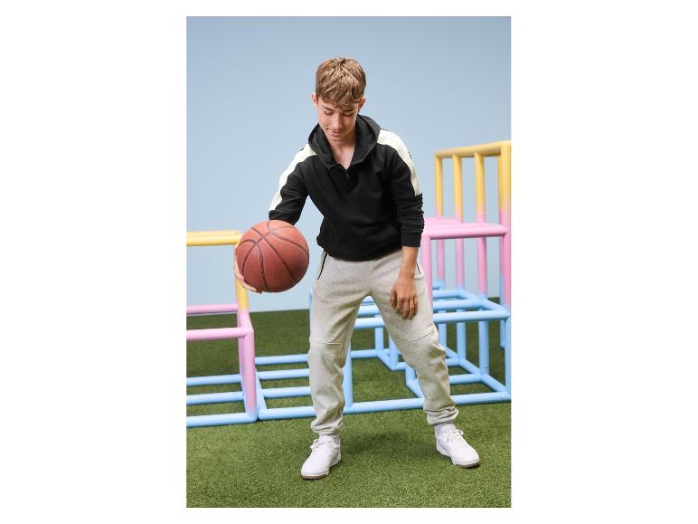 Adolescent en jogging gris et sweat à capuche noir tenant un ballon de basket
