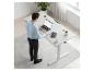Homme debout devant un bureau blanc réglable avec un ordinateur portable, un carnet et une tasse de café.