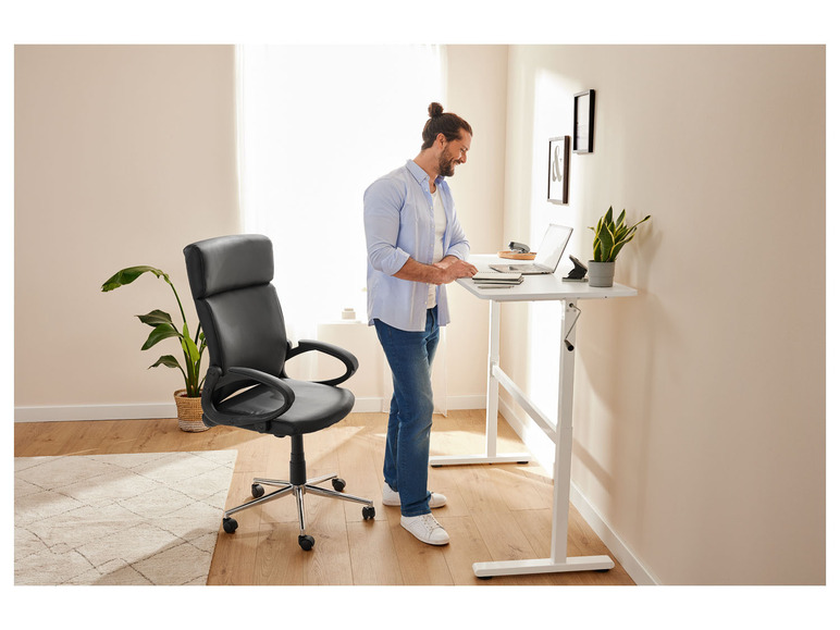 Un homme se tient debout près d'un bureau réglable avec un fauteuil de bureau à côté.