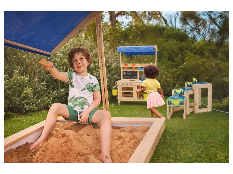 Enfants jouant dans un bac à sable et avec des jouets d'extérieur en bois dans un jardin.