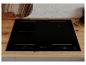 Table de cuisson à induction noire avec quatre zones de cuisson sur un comptoir en bois.