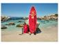 Planche de SUP rouge avec pagaie, sac et pompe sur une plage de sable aux eaux turquoise.