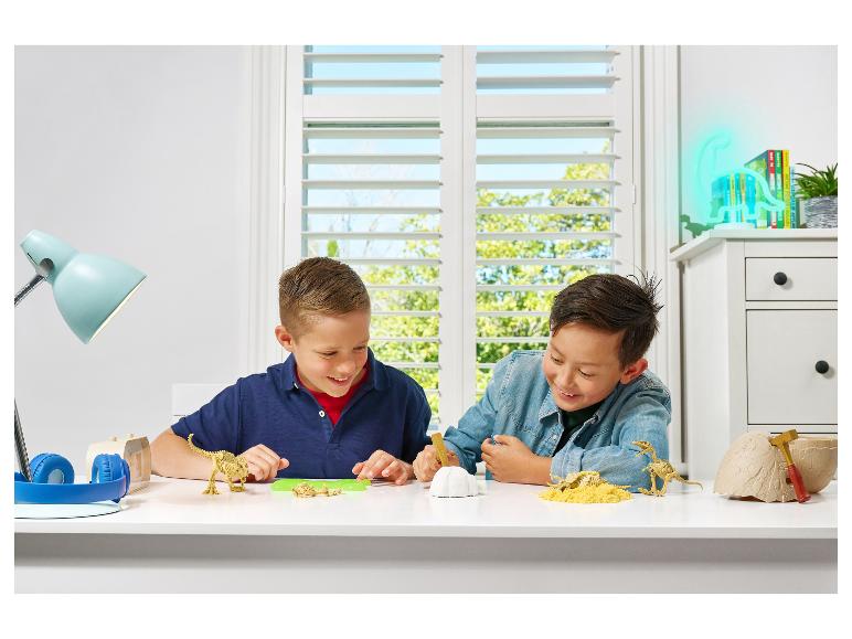 Deux garçons jouent avec des kits de fouille de dinosaures et des squelettes de dinosaures.