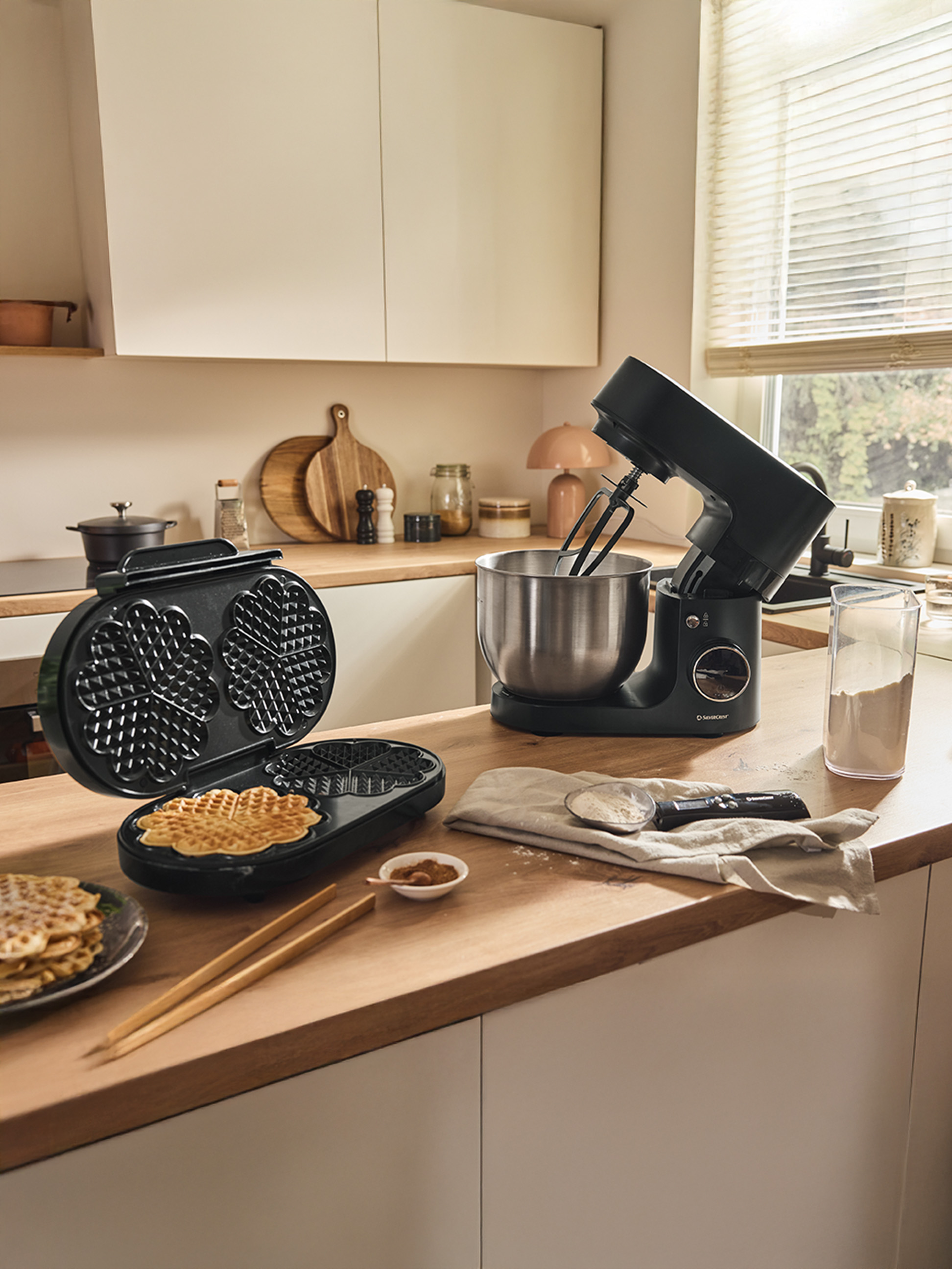 Un gaufrier et un robot pâtissier noir sur un comptoir en bois, avec des gaufres prêtes.
