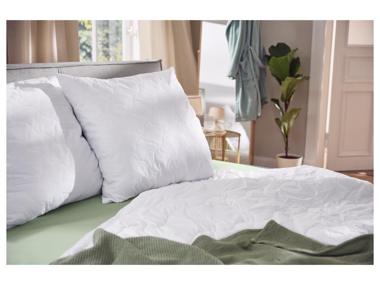 Oreillers et couette blancs sur un lit avec drap et plaid verts.