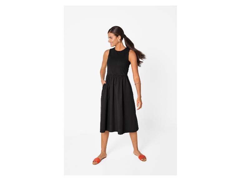 Femme en robe midi noire sans manches avec poches et sandales plates orange.