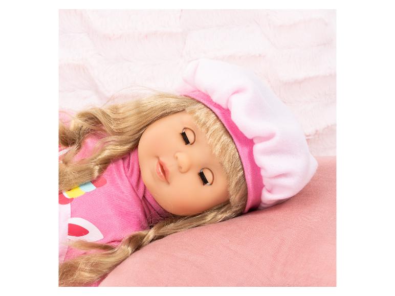 Poupée blonde aux yeux fermés, portant un béret rose et un chemisier rose, dormant sur un oreiller rose