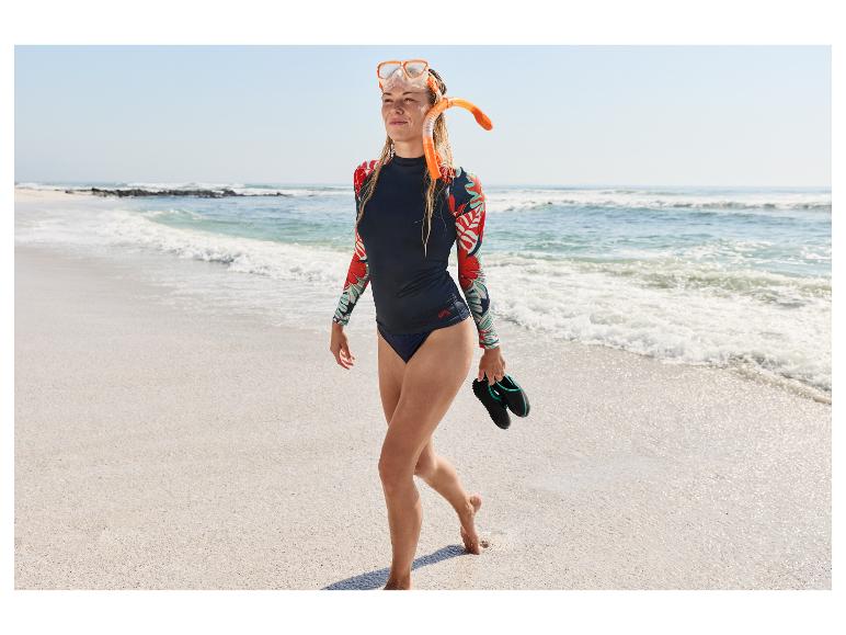 Femme en ensemble de snorkeling CRIVIT et lycra marchant sur une plage de sable.