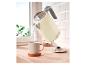 Bouilloire électrique crème versant de l'eau dans une tasse sur un comptoir en bois.