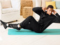 Un homme en tenue de sport noire fait des abdominaux sur un tapis bleu.