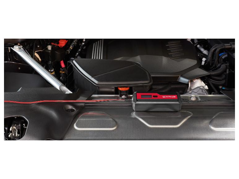 Chargeur de batterie avec des fils rouges connectés dans le compartiment moteur d'une voiture.