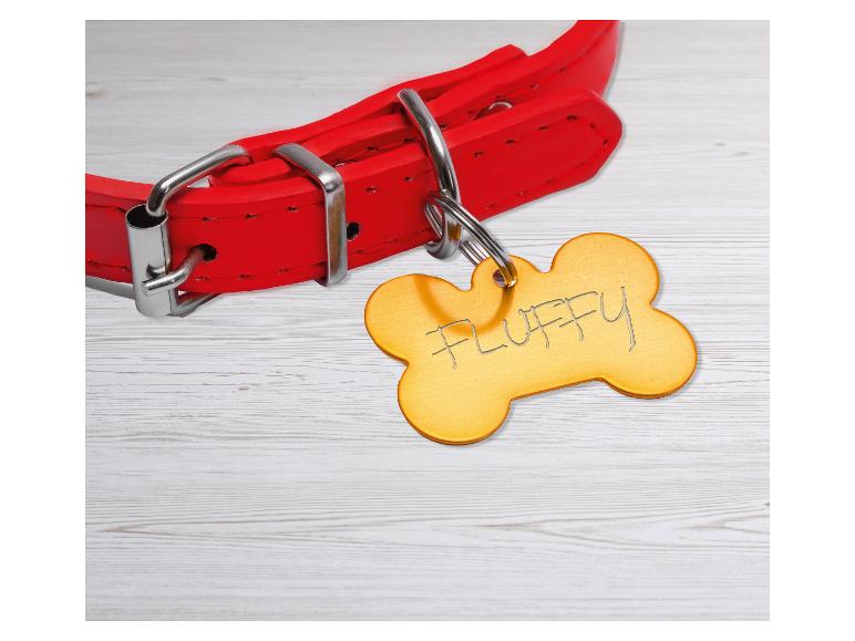 Collier de chien rouge avec une médaille en forme d'os gravée 'FLUFFY' sur une surface en bois.