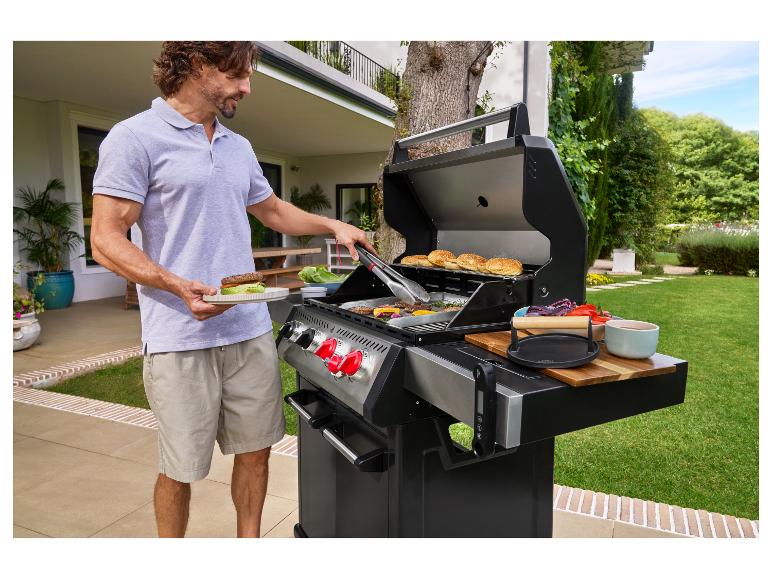 Homme grillant des hamburgers sur un barbecue extérieur, avec pains et légumes.