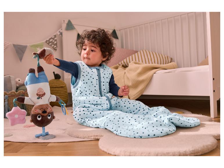 Un bébé dans une gigoteuse à pois bleus joue avec un jouet de loutre.