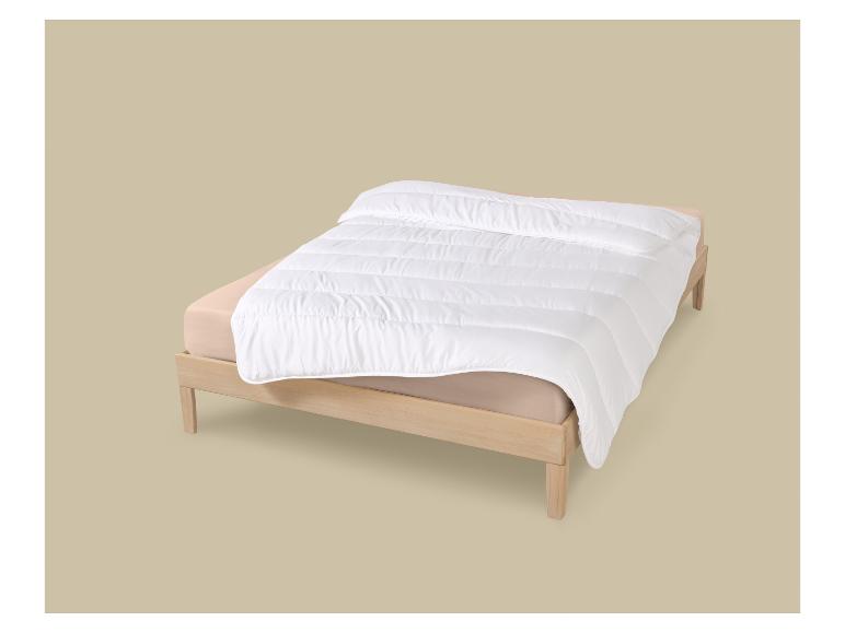 Couette blanche sur un matelas avec des draps beiges sur un lit en bois.