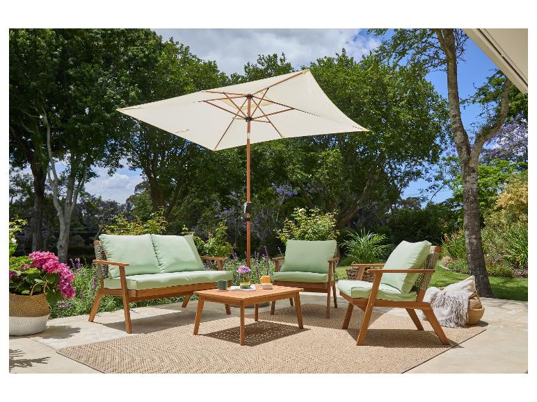 Ensemble de patio extérieur avec mobilier en bois, coussins verts, parasol beige et tapis tressé.