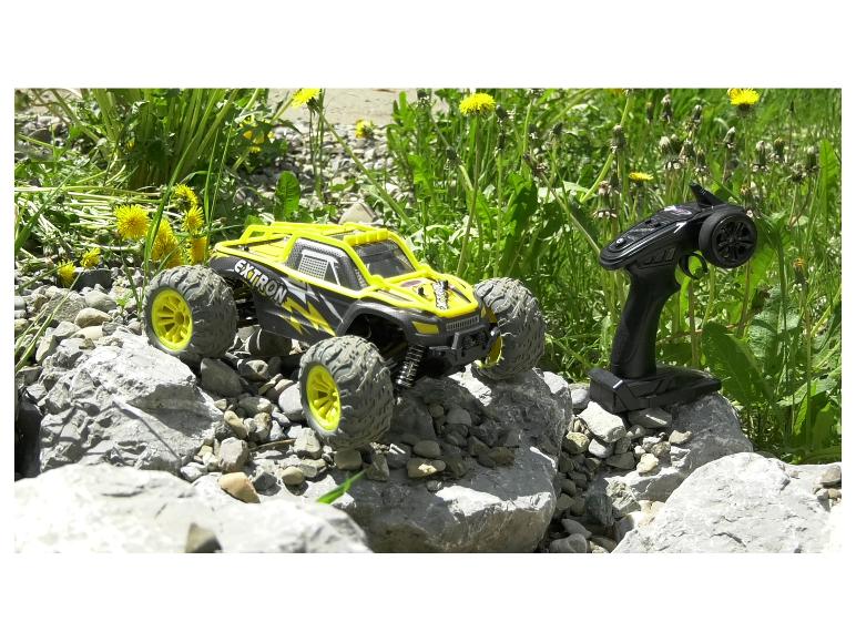 Une voiture télécommandée Extron jaune et noire sur des rochers, avec sa télécommande à côté.
