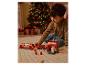 Un enfant joue avec un ensemble de jouets de camion de pompiers en bois sur un tapis, avec un sapin de Noël en arrière-plan.