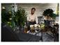 Homme sur balcon avec mobilier d'extérieur, plantes et guirlandes lumineuses.