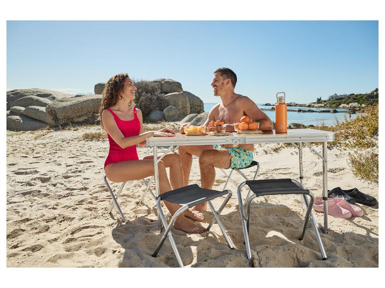Couple sur la plage avec table pliante, fruits et bouteille d'eau.