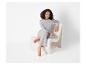 Une femme porte un t-shirt gris et un pantalon, assise sur une chaise blanche.