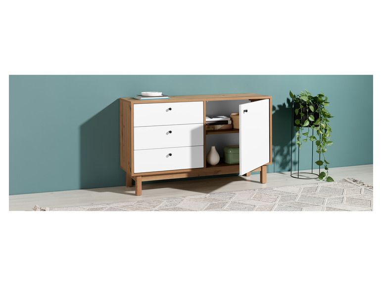 Une commode blanche avec trois tiroirs et une porte, sur un tapis.