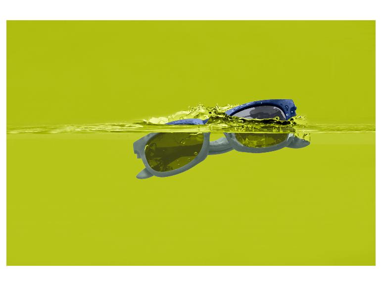 Lunettes de soleil bleues flottant dans l'eau jaune avec des éclaboussures.