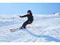Skieur en veste et pantalon de ski noirs, skis et bâtons orange, sur une piste ensoleillée.