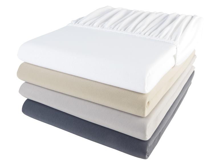 Une pile de quatre draps-housses : blanc, beige, gris et gris foncé.