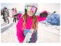 Une fille portant un casque de ski blanc CRIVIT et un masque de ski coloré sur une piste enneigée.